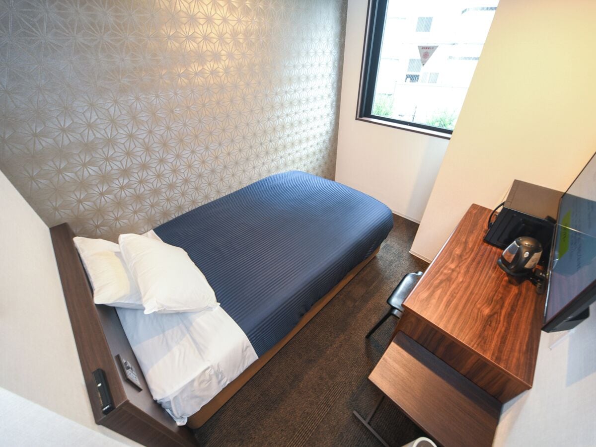 A compact hotel room with a bed, a wooden desk, and a window.