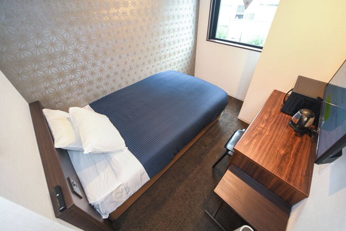 A compact hotel room with a bed, a wooden desk, and a window.