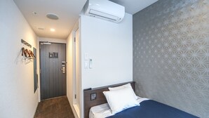 A hotel room with a bed, a wall-mounted air conditioner, a door, and a patterned wall. - HOTEL LiVEMAX Nihonbashi Koamicho (Tokyo)