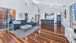 A spacious living area with a dark-colored sofa, a coffee table, and a rug. There is a kitchen area with modern appliances and bar stools.