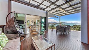 A modern outdoor deck with a glass table, wicker furniture, and a view of the ocean.