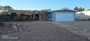 A residential property with a gravel driveway, a brick house, a garage, and a small shed.