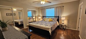 Ein Schlafzimmer mit einem Bett, Nachttischlampen, einem Deckenventilator, einem Spiegel und einer Topfpflanze.