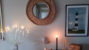 Una habitación con un espejo redondo, un cuadro enmarco de un faro, un florero con luces, una vela y un cofre de madera.