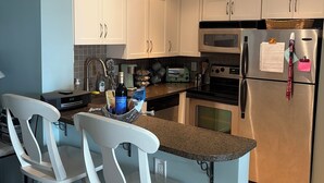 Una cocina con armarios blancos, un refrigerador de acero inoxidable, un microondas y una encimera de granito.