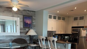 Una cocina moderna con armarios blancos, una zona de comedor con sillas de madera y un sofá blanco con un cojín colorido.