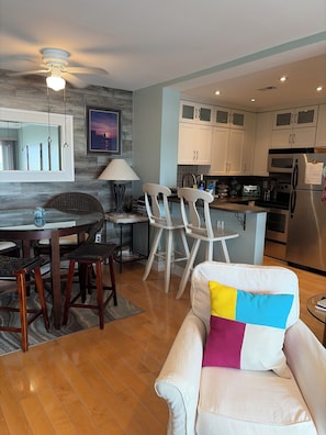 A modern kitchen with white cabinets, a dining area with wooden chairs, and a white sofa with a colorful pillow. - >>Exceptional Updated Condo w Waterfront Views All Rooms-Walk to Town, Ferry<< (Port Clinton)