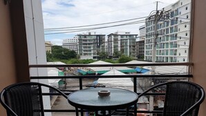 A balcony with two wicker chairs and a small round table, overlooking a cityscape with modern buildings and a street below. - Secrets Pattaya (Pattaya)