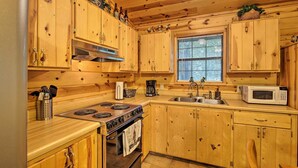 Cocina tipo cabaña de madera con estufa, horno, microondas, pileta y armarios de madera.