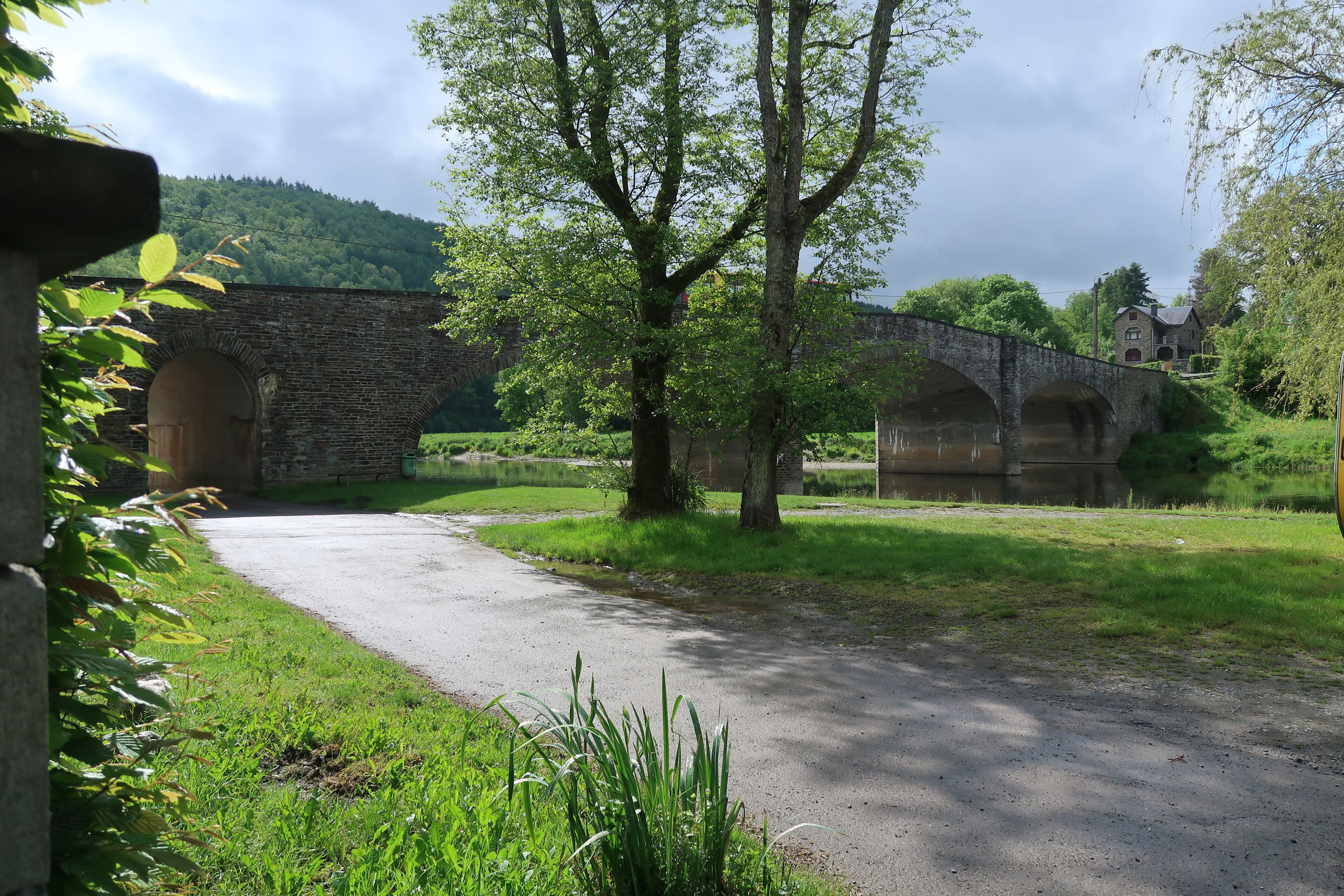 Un pont de pierre enjambant une rivière, entouré de verdure et bordé d’un bâtiment en pierre.