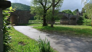 Un pont de pierre enjambant une rivière, entouré de verdure et bordé d’un bâtiment en pierre.