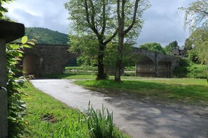 Un ponte di pietra che scavalca un fiume, immerso nel verde e con un edificio in pietra sullo sfondo.