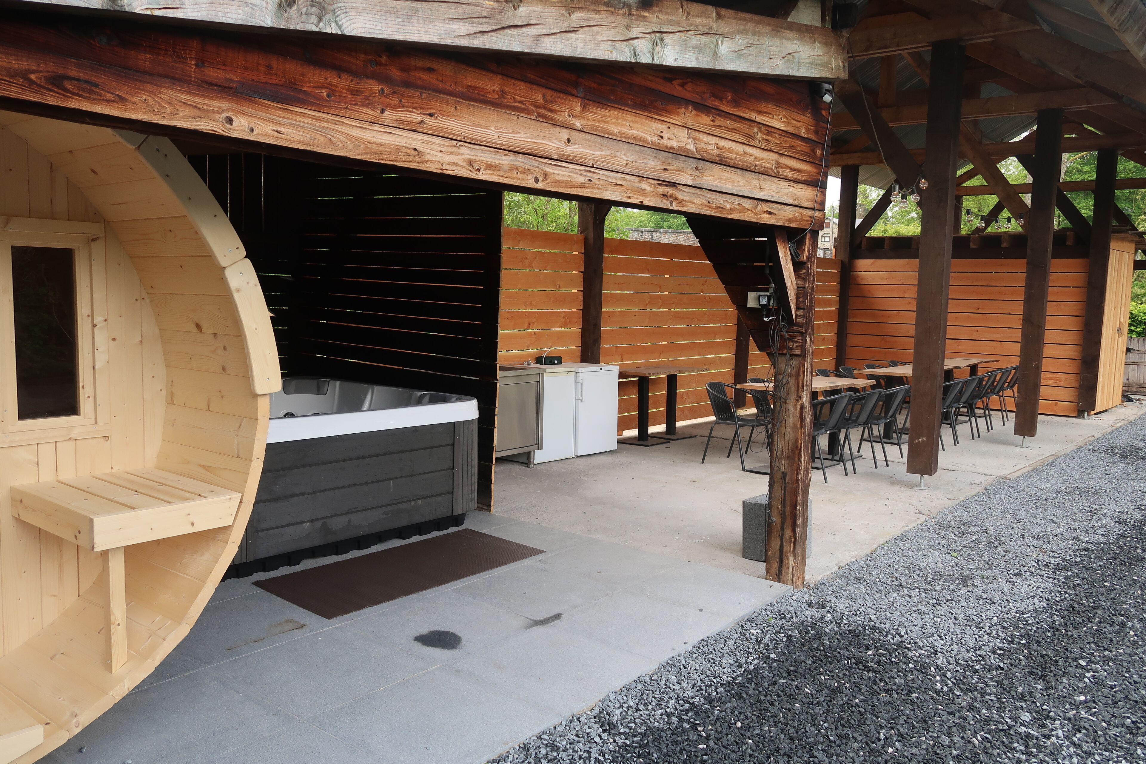 Un espace extérieur aménagé avec un bain à remous en bois, un banc en bois et une table avec des chaises.