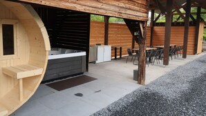 Un espace extérieur aménagé avec un bain à remous en bois, un banc en bois et une table avec des chaises.