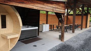 Un espace extérieur aménagé avec un bain à remous en bois, un banc en bois et une table avec des chaises.