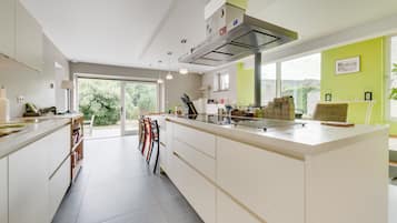 Une cuisine moderne dotée d’un grand îlot central, de meubles blancs et offrant une vue sur la verdure environnante.
