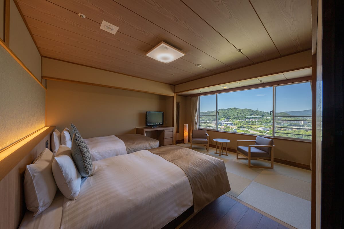 Habitación de hotel con una cama grande, un escritorio con televisor, una silla y vistas del paisaje.