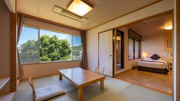 A room with tatami flooring, a wooden table, a bed, and a view of greenery outside.