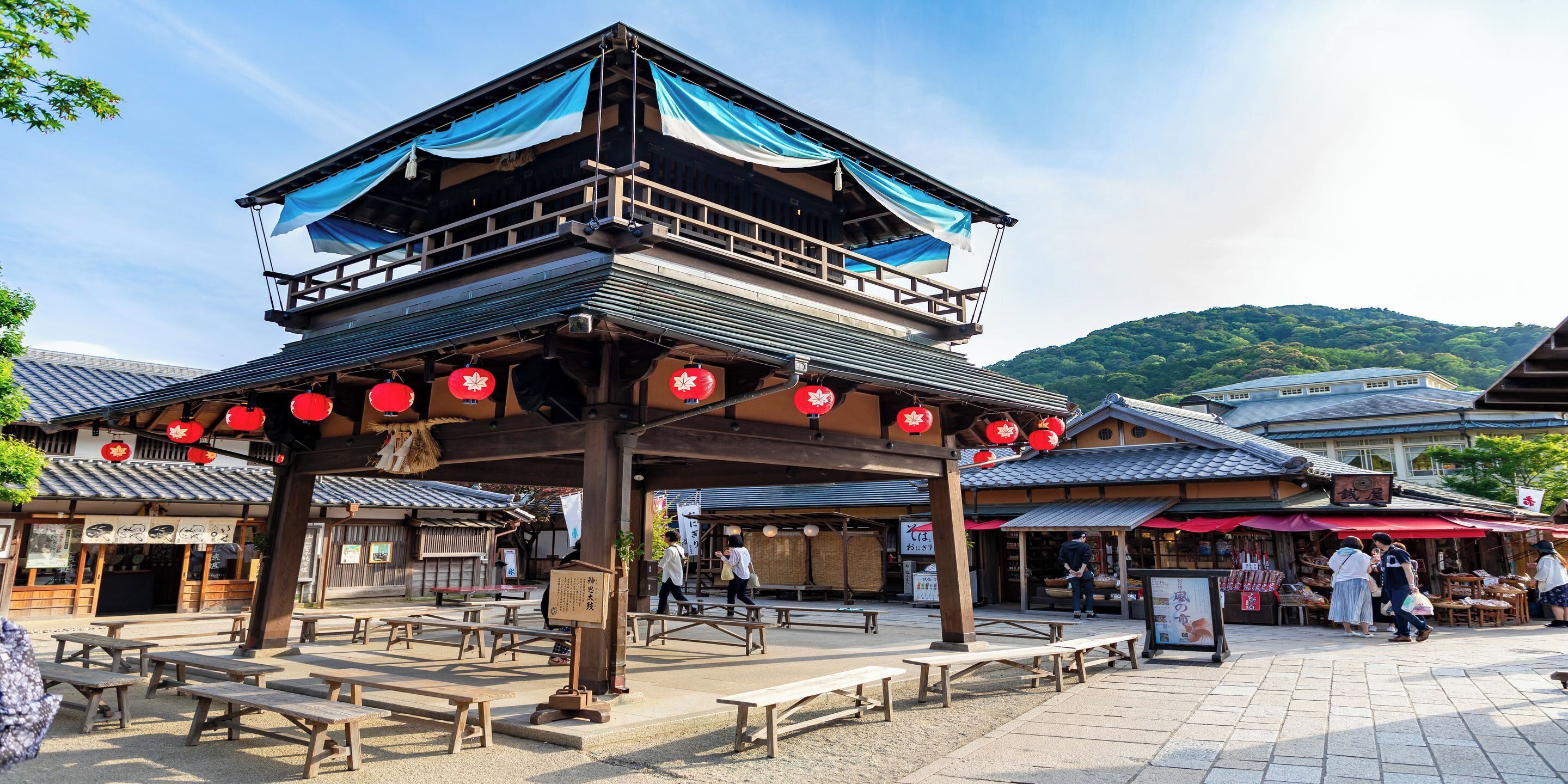 A traditional Japanese building with a wooden structure, outdoor seating, and red lanterns.