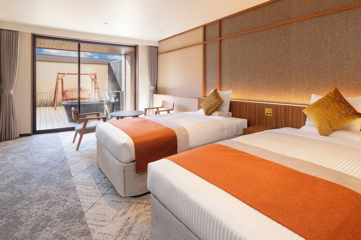Una habitación de hotel con dos camas, un área de descanso con mesa y sillas, y vistas al exterior.