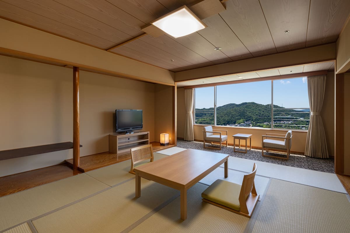 Habitación de hotel con suelo de tatami, televisor, mesa de comedor y vista a la montaña.