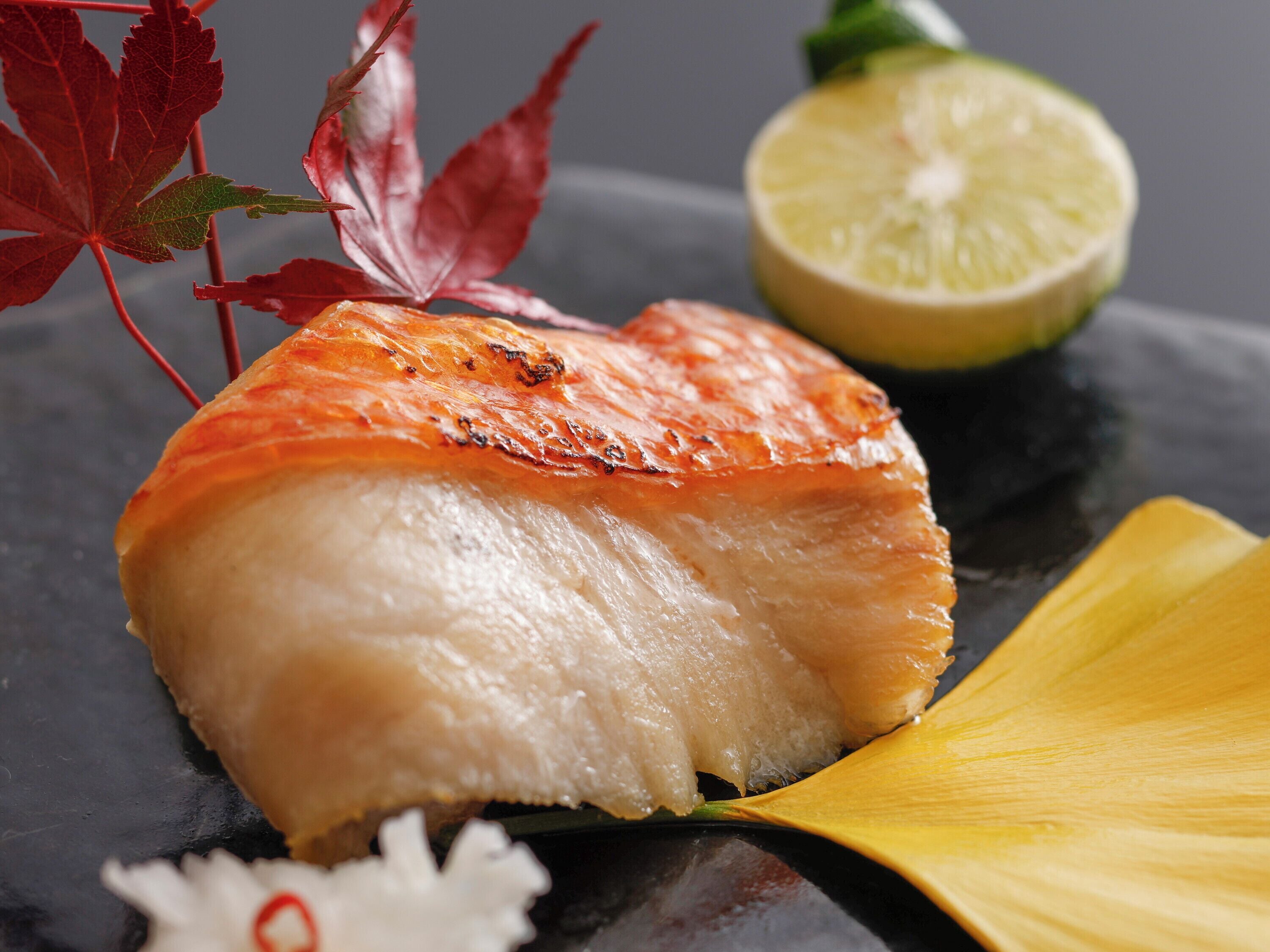A salmon fillet with a slice of lime and decorative leaves on a dark surface.