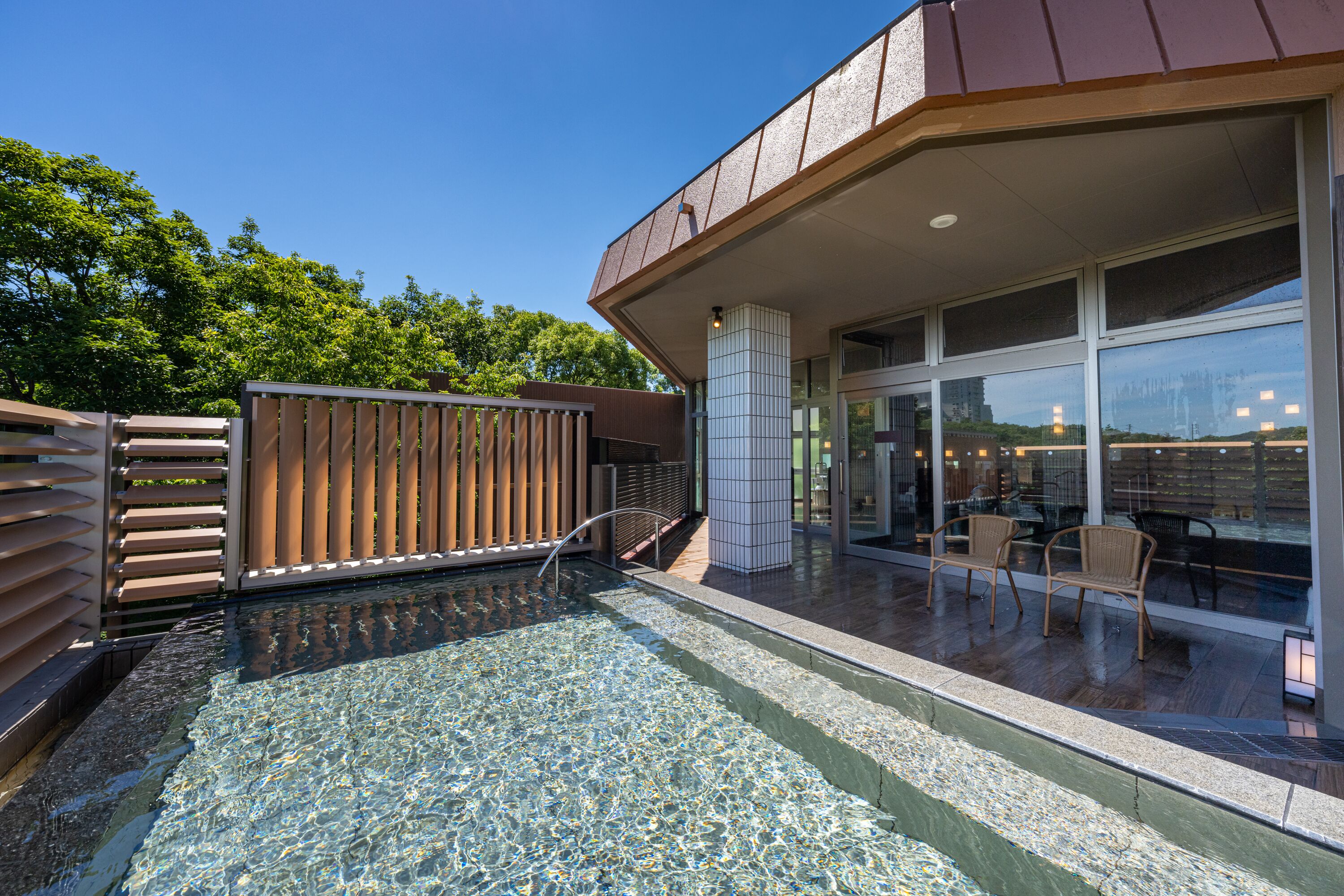 A modern building with a glass facade, a pool area with clear water, and outdoor seating.