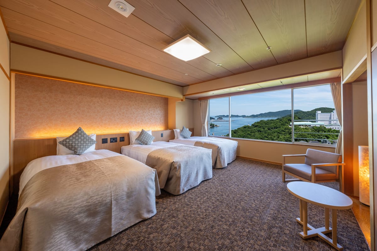 Habitación de hotel con tres camas, una mesita y vistas al mar.