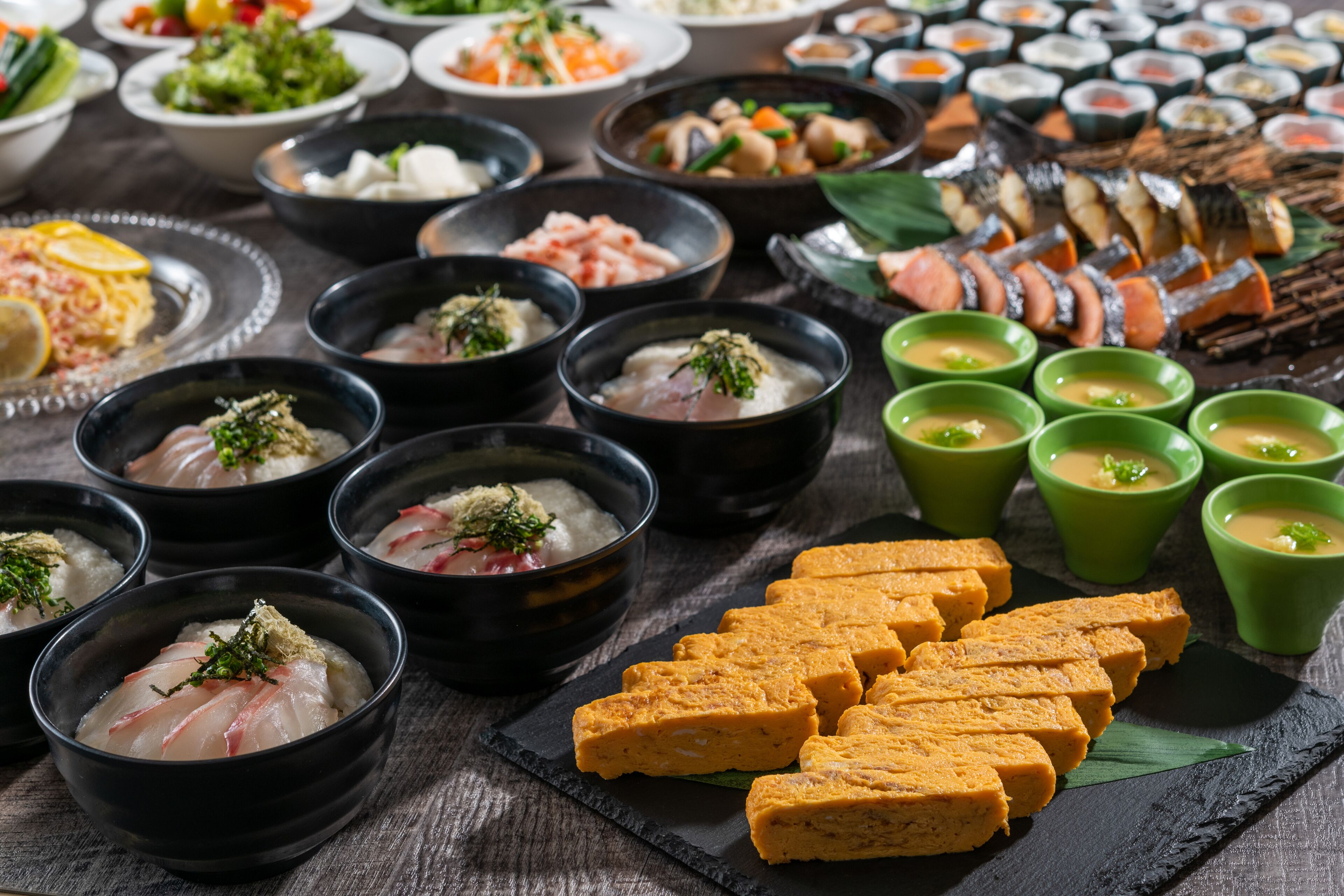 A variety of dishes including sashimi, tofu, and sushi on a wooden table.