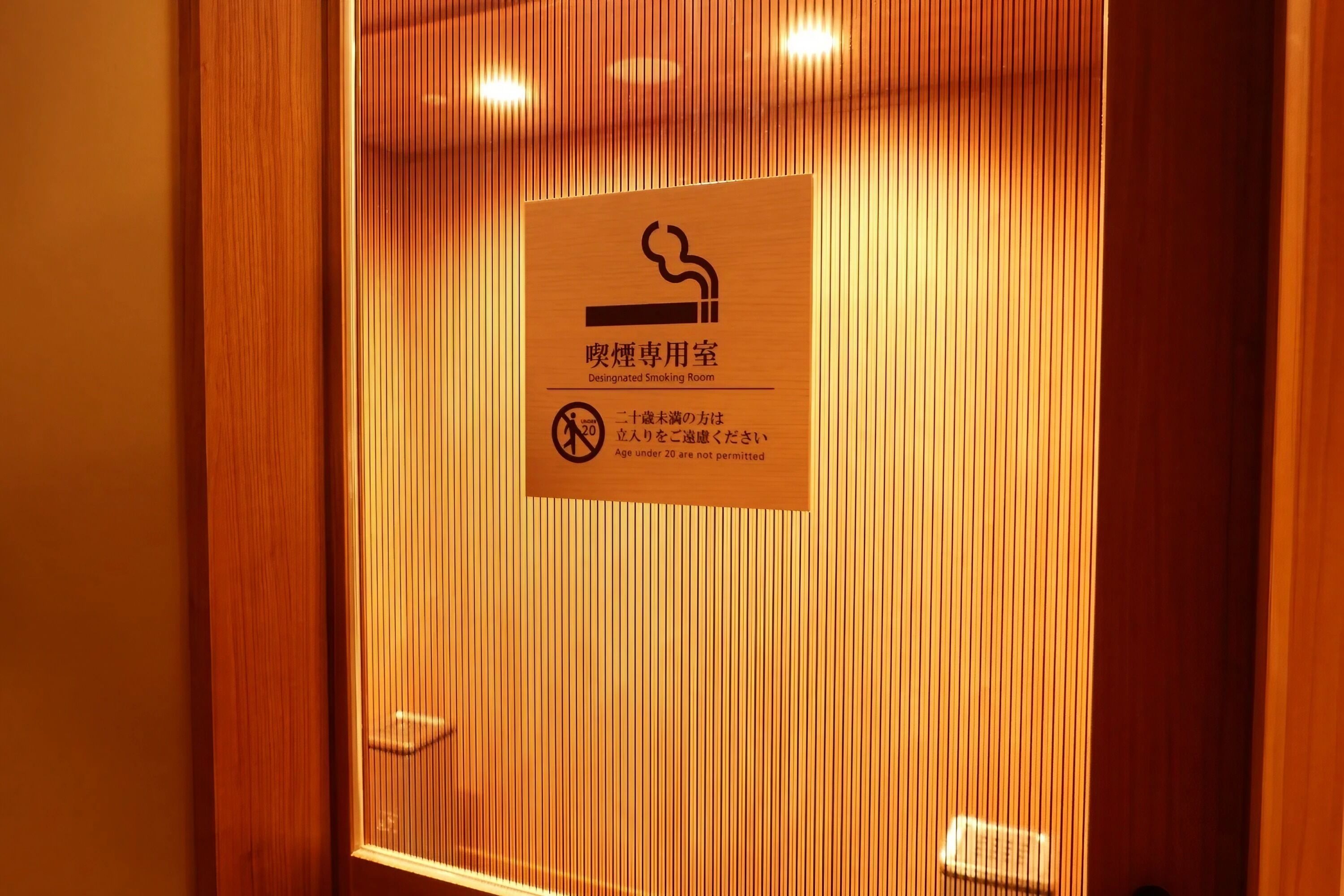 A sign indicating a designated smoking room with a no-smoking symbol and a note that individuals under 20 are not permitted.