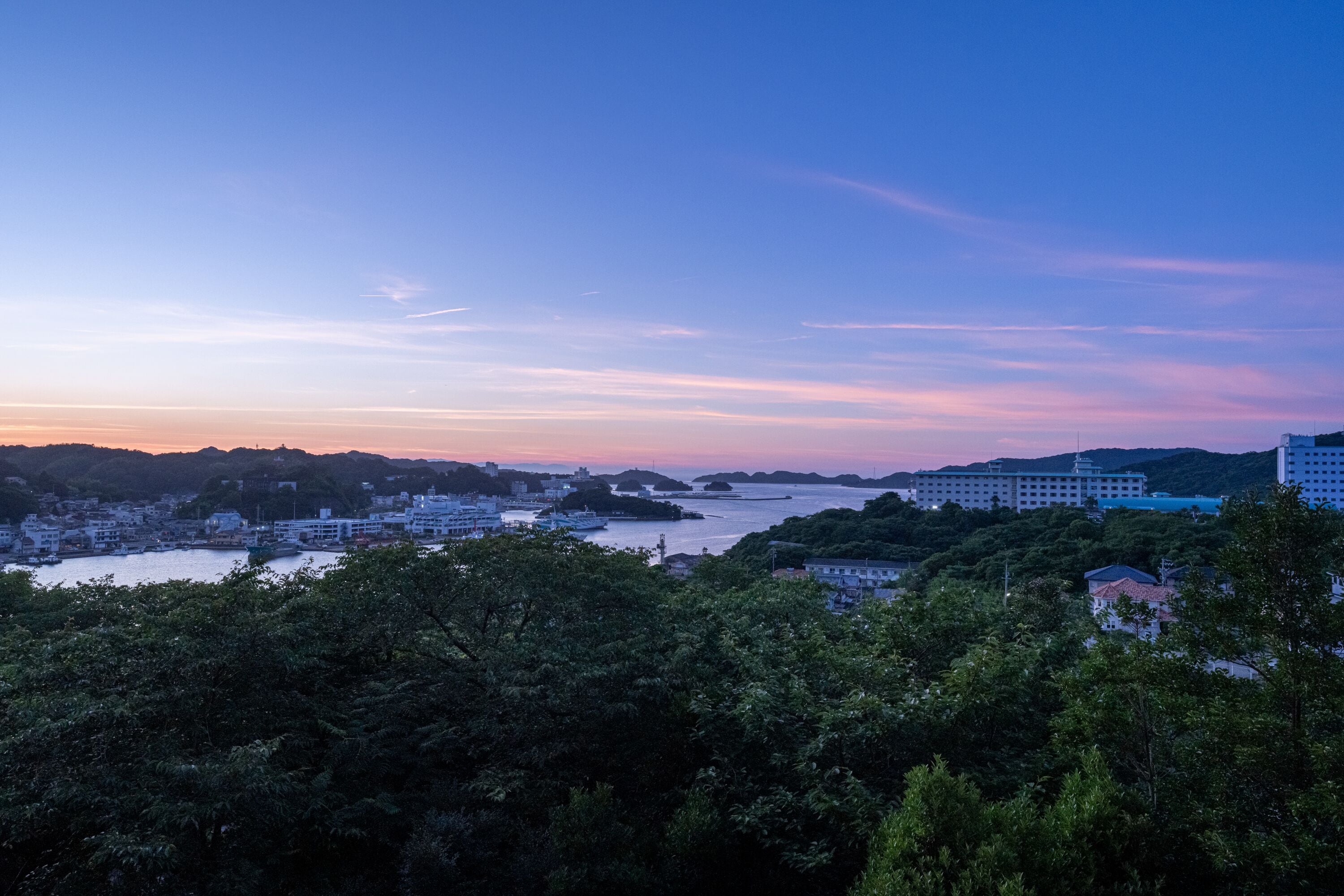A coastal cityscape with buildings, a river, and hills.