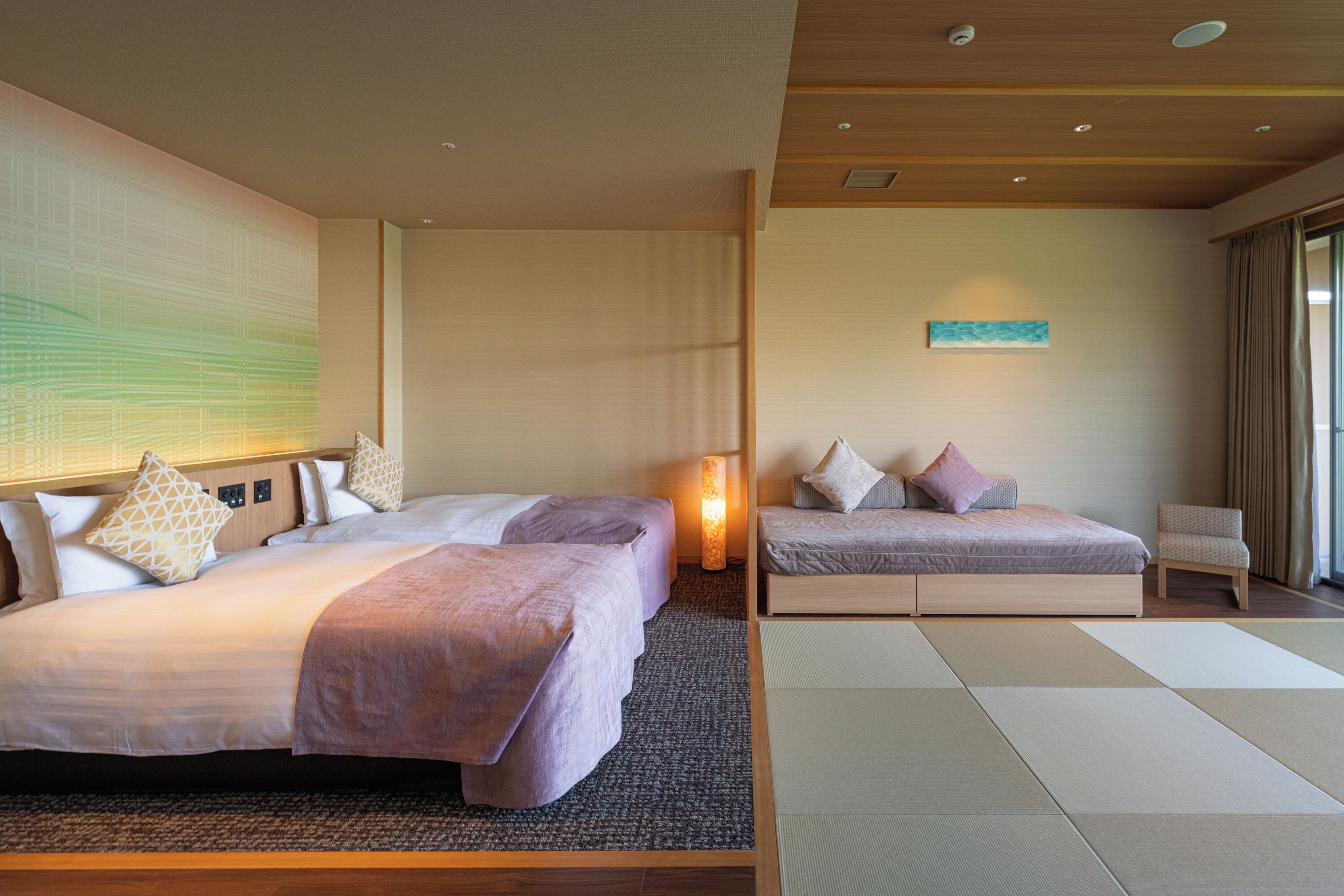 A hotel room with two beds, a sitting area, a large window, and a wall-mounted artwork.