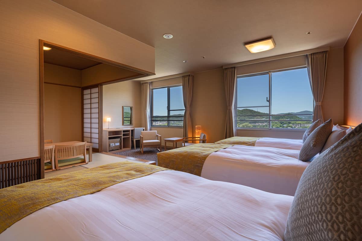 Habitación de hotel con dos camas, un escritorio, una silla y vistas al exterior.