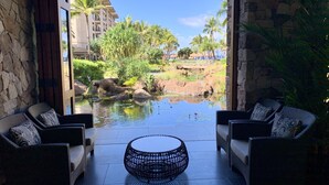 Blick auf einen Poolbereich mit zwei Korbsesseln und einem runden Tisch, umgeben von Steinmauern und einer Aussicht auf ein Resort.