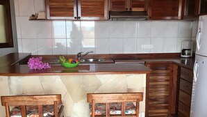 A kitchen with a tiled backsplash, wooden cabinets, a sink, a coffee maker, and two wooden stools.