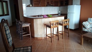 A kitchen with a central island, wooden chairs, a white refrigerator, and a dining table with chairs.