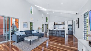 A spacious living area with a dark grey sofa, a coffee table, and a rug. A kitchen with modern appliances and bar stools is visible in the background. - Mandalay Escape Serenity and Pool (Mandalay)