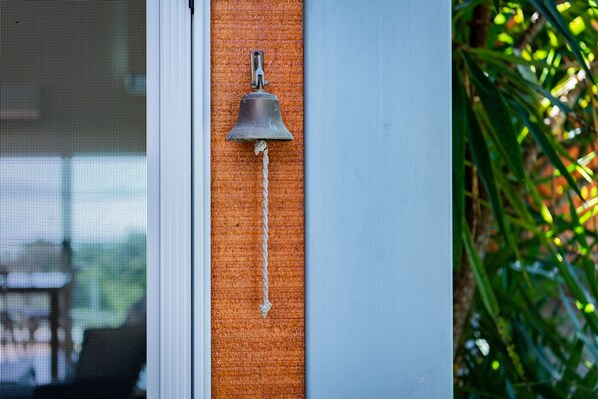 A metal bell mounted on a textured orange wall, with a rope hanging from it. - Mandalay Escape Serenity and Pool (Mandalay)