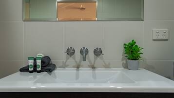Un bany amb un rentapans blanc, tres aixetes, un mirall i una planta en test.