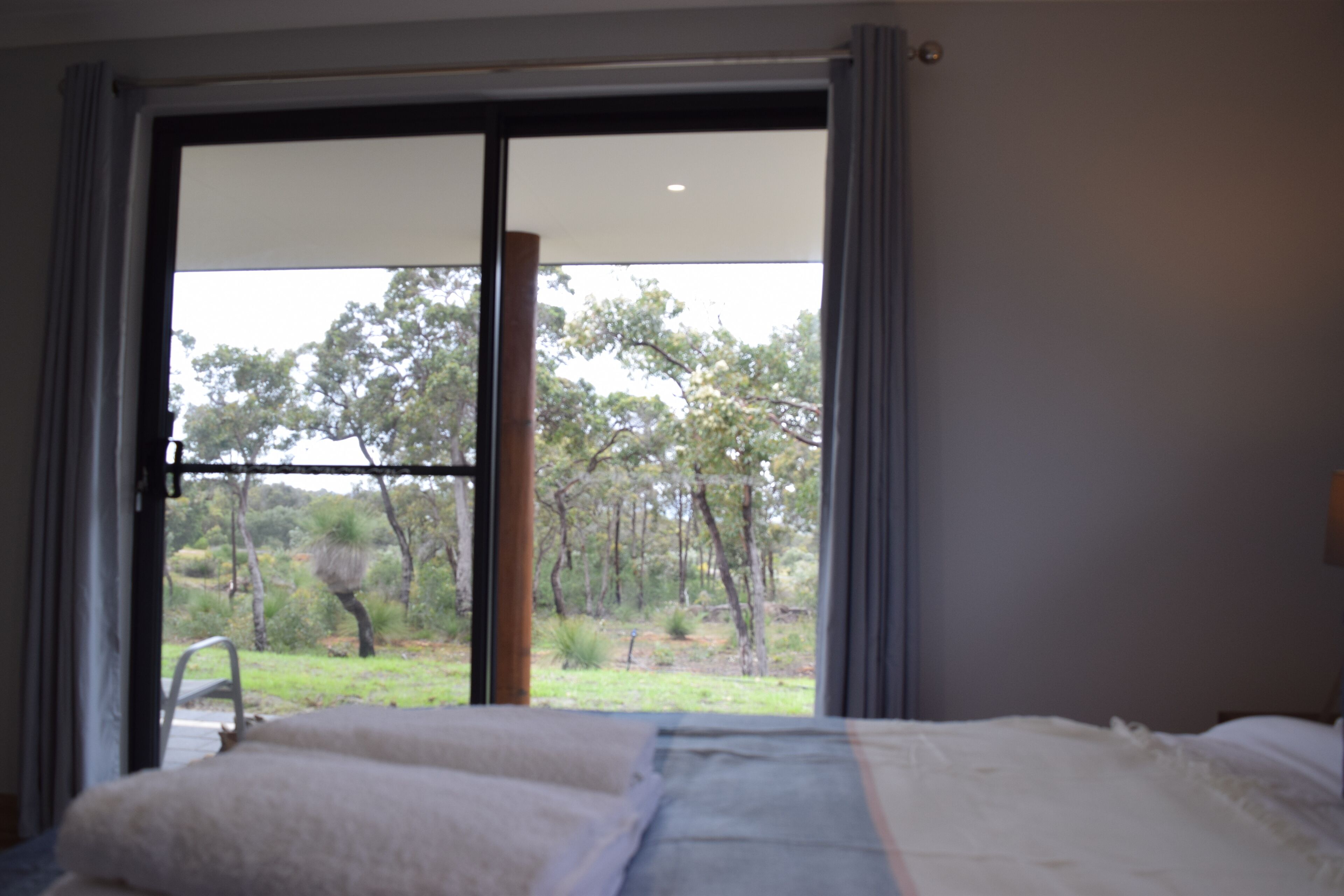 Een slaapkamer met een groot raam, een bed en uitzicht op bomen en gras.