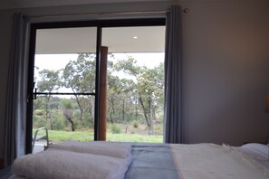 Un dormitorio con un ventanal grande, una cama y vistas a árboles y césped.