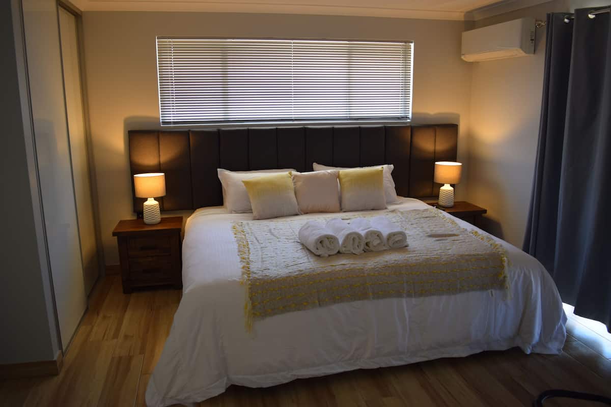 A neatly made bed with a white bedspread and pillows, two bedside lamps, and a window with blinds.