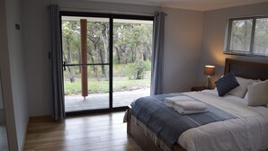 A bedroom with a large sliding glass door leading to a balcony, a bed with a blue and white bedspread, and a nightstand with a lamp. - Eagle Bay House (Eagle Bay)