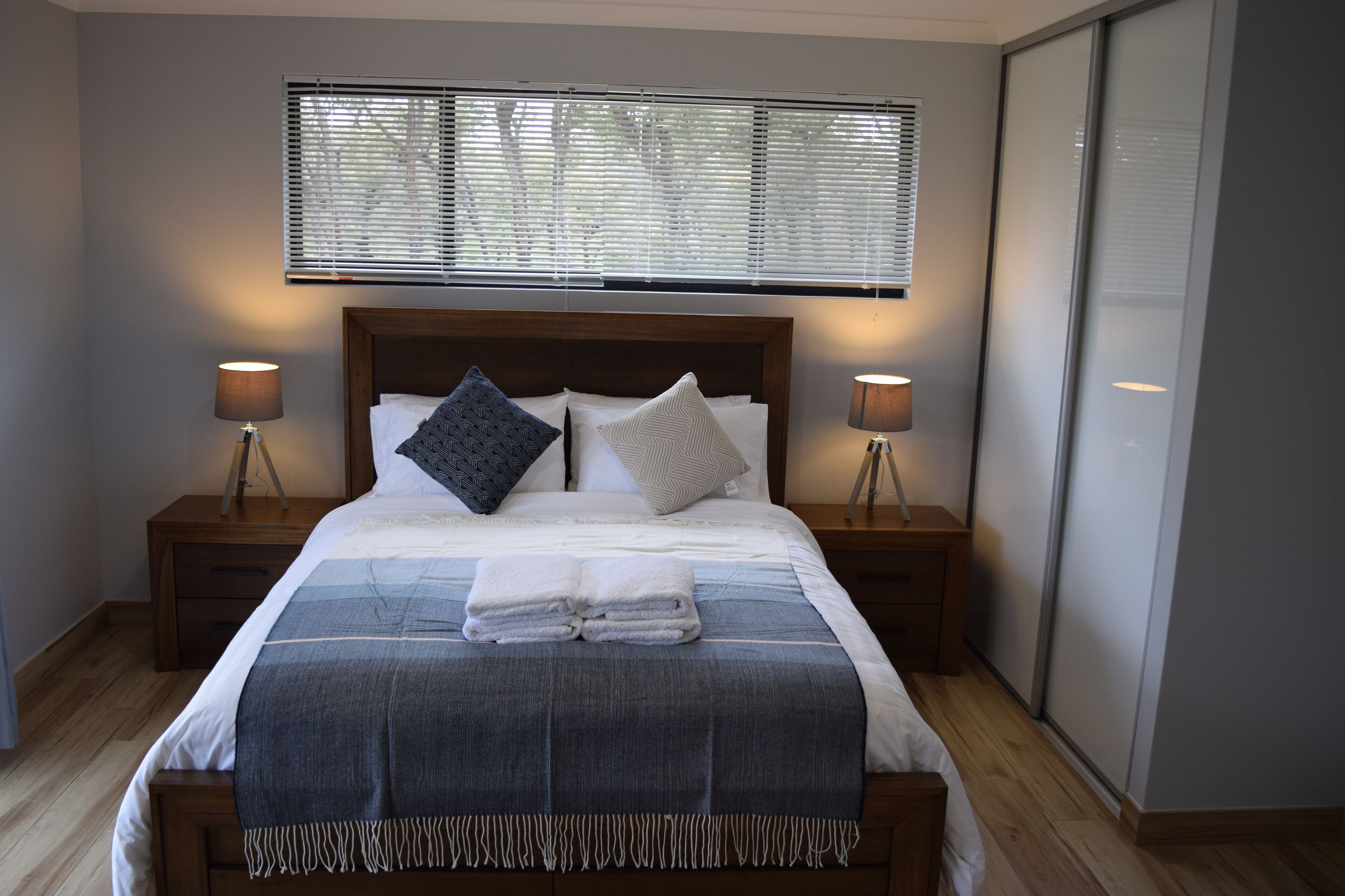 A neatly made bed with a blue and white striped blanket, two bedside lamps, and a window with blinds.