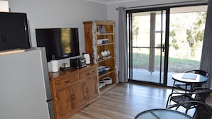 A kitchen with a refrigerator, stove, and microwave, a wooden cabinet with shelves, a television, and a glass table with chairs. - Eagle Bay House (Eagle Bay)