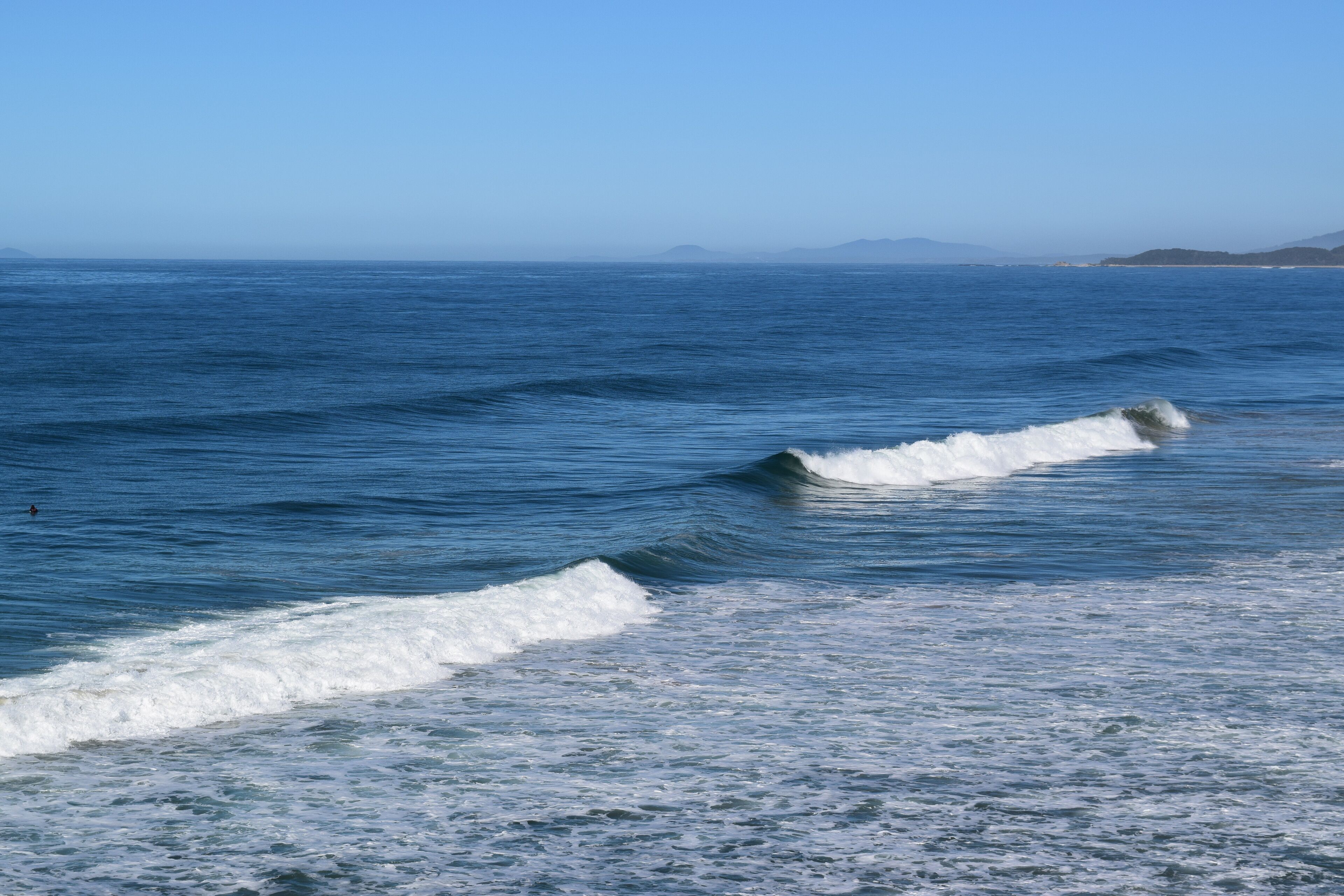 A coastal view with waves and distant landforms.