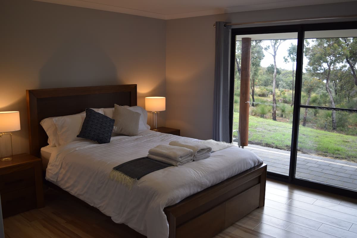 A bedroom with a large bed, two bedside tables with lamps, a view of a garden through a sliding glass door.