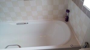 Una vasca da bagno bianca con un rubinetto cromato e un mancorrente, affacciata su una parete piastrellata con motivo a scacchi.