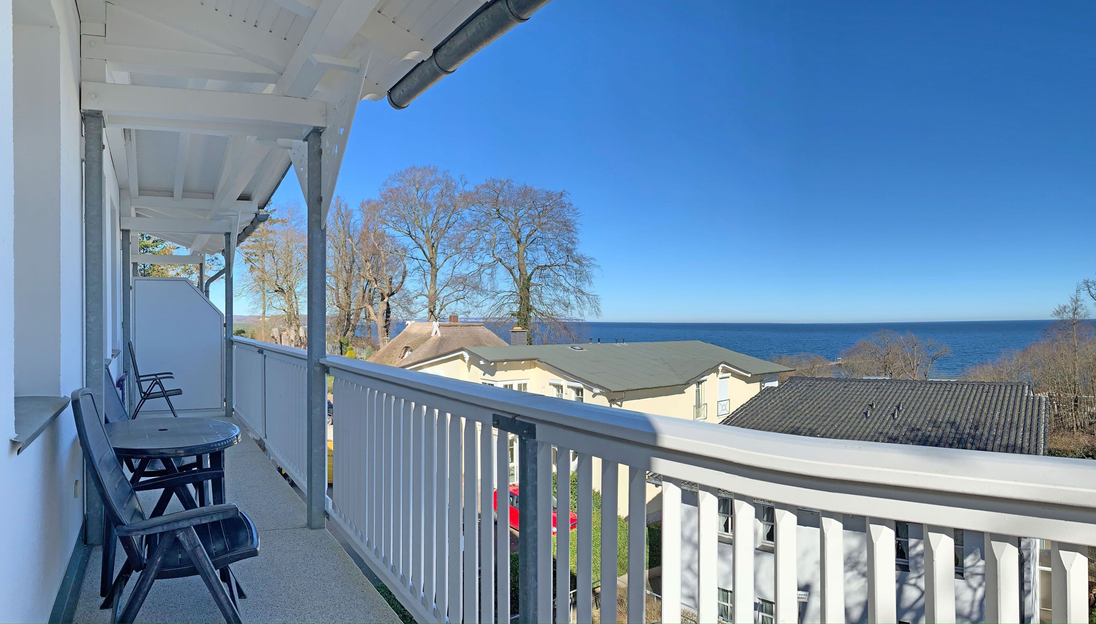 A balcony with a view of the sea, a table, and chairs.