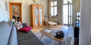 A living room with a grey sofa, a wooden cabinet, a wooden chair, a coffee table, and a window with curtains.